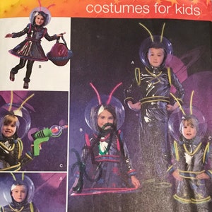 May include: Simplicity sewing pattern number 2796 for kids costumes. The pattern includes instructions for making four different space-themed costumes. The costumes feature a silver, black, and yellow color scheme with a futuristic design. The pattern is for sizes 3-8.