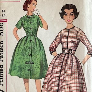 May include: Vintage Simplicity sewing pattern, number 3072, featuring illustrations of two dresses. One dress is green with buttons, the other is a red and white plaid. The pattern includes measurements for Miss Size 14, Bust 34.