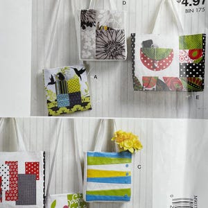 May include: A McCall's sewing pattern for "EASY stitch 'n save" featuring multiple small tote bags. The bags showcase diverse fabric designs, such as floral, geometric, and patchwork. Each bag has white handles and is presented against a light-coloured background.
