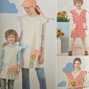 May include: Simplicity sewing pattern featuring aprons for adults and children. The aprons have floral and gingham designs. The pattern includes sizes S-L. The image shows the aprons being worn.