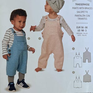 May include: A Burda Kids sewing pattern envelope for pants with braces, featuring two children wearing blue and peach-colored overalls. The package displays the text Burda kids, Traegerhose, Pants with braces, Salopette, and sizes EUR 56-98, US 1M-3.