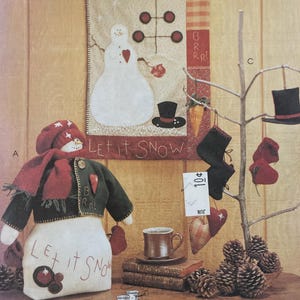 May include: McCall's Crafts pattern envelope featuring a snowman design. The image shows a snowman doll, a snowman wall hanging, and decorative elements like hearts and pinecones. Text includes "Let it Snow" and "Hanging by a Thread".
