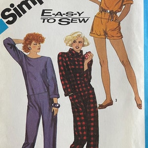 May include: A vintage Simplicity sewing pattern envelope, featuring illustrations of three different outfits: a purple jumpsuit, a red and black plaid pantsuit, and an orange shorts set. The envelope has the text "Simplicity" and "E-A-S-Y TO SEW".