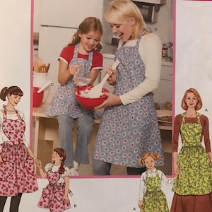 May include: Simplicity sewing pattern 3949 featuring aprons in various styles. The pattern includes images of aprons with floral and heart designs, suitable for adults and children. The pattern's size range is A, S, M, L, and S/M/L.