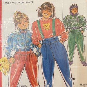Peut inclure: Un patron de couture pour pantalons, avec des illustrations de trois enfants portant différents styles de pantalons. Le numéro du patron est 6192. Les tailles sont 86+92+104+116+128+140, correspondant aux tailles 2+3+4+6+7+10.