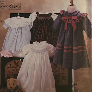 May include: Simplicity sewing pattern number 7644 for sizes AA (2-4). The pattern includes instructions for making four different baby dresses: a white dress with a lace collar, a plaid dress with a white collar, a blue dress with a lace collar and a white dress with a smocked bodice.