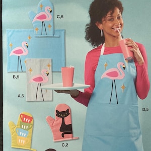 May include: McCall's sewing pattern featuring a flamingo-themed apron, oven mitts, and dish towels. The apron is light blue with a pink flamingo design. Other patterns include a black cat and a cocktail glass.
