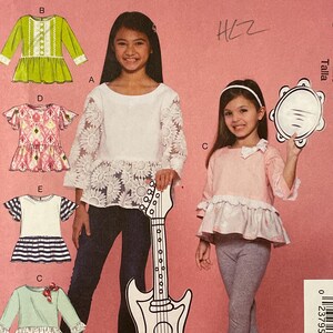 May include: A McCall's sewing pattern envelope, M7559, featuring illustrations of girls' tops. The envelope is pink with the McCall's logo and size information. The pattern includes various top designs with different sleeve styles and embellishments.