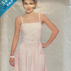 May include: A vintage sewing pattern titled "See & Sew 5294" featuring a light pink button-down dress with pockets. The dress has a square neckline and spaghetti straps. The pattern cover shows a woman wearing the dress.