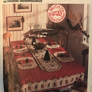 May include: A red and white tablecloth with a festive holiday design. The tablecloth is laid on a table with a runner and placemats. There are glasses and candles on the table. The image is from McCall's Home Decorating, Dining Essentials, pattern number 8438.