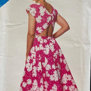 May include: A vintage sewing pattern for a dress with a floral print. The dress is a vibrant pink with white daisy-like flowers. The pattern is labeled "See & Sew" and includes the size range A (6-8-10).