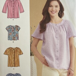 May include: Simplicity sewing pattern S9782. The pattern features four blouse designs, including a pink long-sleeve blouse, a floral print short-sleeve blouse, a mustard yellow short-sleeve blouse, and a blue patterned short-sleeve blouse. The pattern is designed and printed in the USA.