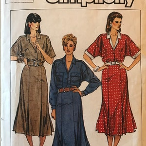 Peut inclure: Enveloppe de patron Simplicity avec des illustrations de trois modèles de robes chemisiers. Les robes sont marron, bleu et rouge à pois blancs. L'enveloppe porte le numéro 8 et le logo Simplicity.