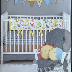 May include: Simplicity sewing pattern S8939 for nursery items including a crib bumper with a woodland animal print, a bunting banner, a grey crib skirt, a grey textured blanket, and two round plush pillows shaped like a sun and a crescent moon.