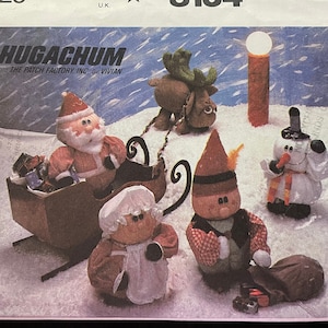 May include: A vintage McCall's sewing pattern for making a set of Christmas-themed plush toys. The pattern includes instructions for making a Santa Claus, a snowman, a reindeer, and a little girl. The pattern is titled "Hugachum" and is from the Patch Factory, Inc. by Vivian. The pattern number is 8134.