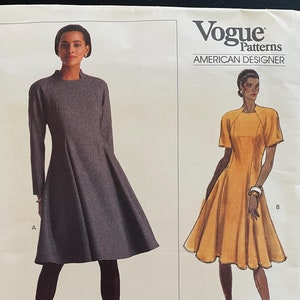 May include: Vogue Patterns sewing pattern featuring two dress designs by Geoffrey Beene. The pattern includes illustrations of a long-sleeved grey dress and a short-sleeved yellow dress. The pattern is labelled "American Designer" and "Easy/Facile".