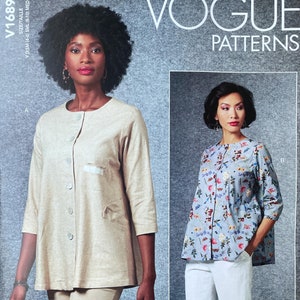 May include: Vogue Patterns V1689 sewing pattern featuring two women modeling tops. One top is beige with buttons and pockets, the other is blue striped with floral accents. The pattern includes sizes XS to Medium.