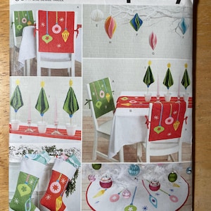 May include: A Simplicity sewing pattern with Christmas decorations. The pattern includes designs for chair covers, a table runner, tree ornaments, Christmas stockings, and a tree skirt. The colour palette includes red, green, white, and gold accents. The text "easy-to-sew" is visible.