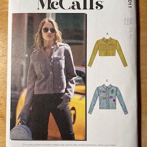 May include: McCall's sewing pattern M8011. The pattern features a woman wearing a gray jacket. The pattern includes multiple view options with simple instructions. Designed and printed in the USA.
