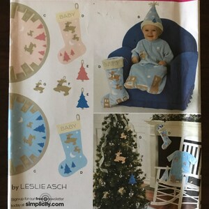 May include: A Simplicity sewing pattern for a baby's Christmas outfit, including a stocking, a hat, and a sleeper. The pattern number is 2489. The pattern includes instructions for making a Christmas tree, a stocking, and a sleeper.