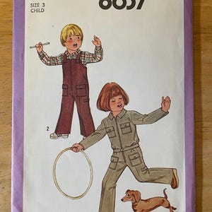 May include: Simplicity sewing pattern number 8637 for children's clothing. The pattern includes instructions for making two different styles of dungarees. The first style is a brown pair of dungarees with a plaid shirt. The second style is a green pair of dungarees with a long-sleeved shirt. A small dog is included in the image.