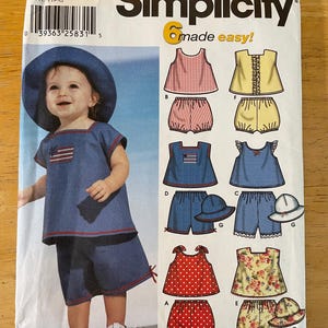 May include: Simplicity sewing pattern number 7239 for making six different baby girl outfits. The pattern includes a denim overall dress with a red, white, and blue American flag design, a red and white striped tank top with matching shorts, a yellow tank top with matching shorts, a red polka dot tank top with matching shorts, a floral print tank top with matching shorts, and a blue gingham tank top with matching shorts. The pattern is for sizes XXS, XS, S, M, and L.