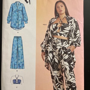 May include: Simplicity sewing pattern R11772 featuring a three-piece outfit. The pattern includes a long-sleeved button-down shirt, wide-leg pants, and a halter top. The outfit is shown in a black and white floral print. Size U.S. 20W-28W.