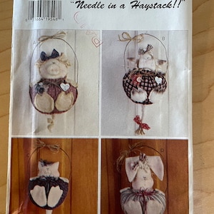 May include: A sewing pattern for four different stuffed animal ornaments. The pattern is called "Needle in a Haystack!" and includes a pig, a cat, a bunny, and a cow. The pattern is from Butterick and is size O/S.