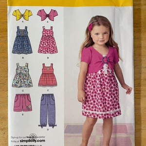 May include: Simplicity sewing pattern number 2268 for girls' dresses and tops. The pattern includes a dress with a bow, a dress with a ruffle, a pair of shorts, and a pair of pants. The pattern is for sizes 3, 4, 5, 6, 7, and 8.