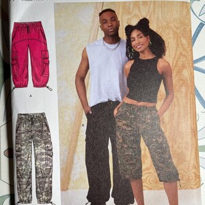 May include: Simplicity pattern S9959 features cargo pants in sizes XS-XXL. The pattern includes two styles: one in a vibrant red and the other in a camouflage print. The package is designed and printed in the USA.