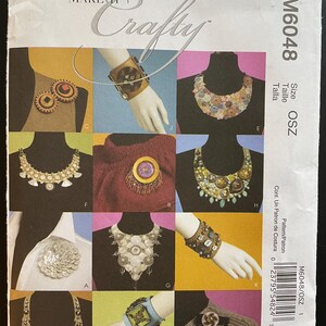 May include: A pattern sheet for making jewelry, featuring nine different designs for necklaces and bracelets. The designs include a variety of materials, such as buttons, beads, and fabric scraps. The pattern sheet is titled "Make It Crafty" and is from McCall's.