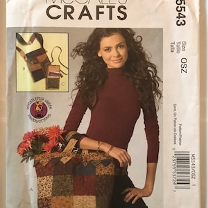 May include: A sewing pattern for a patchwork tote bag and a small crossbody bag. The pattern is from McCall's Crafts and is size OSZ. The tote bag is made of different fabrics with a patchwork design. The crossbody bag is made of a striped fabric with a brown leather trim.