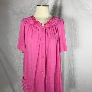 May include: A pink button-up top with short sleeves and a floral embroidered neckline.