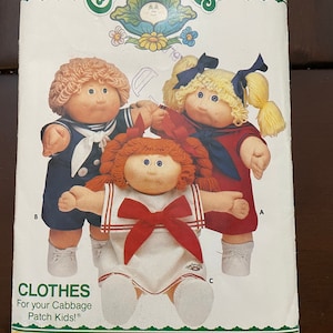 May include: A vintage sewing pattern for Cabbage Patch Kids clothes. The pattern is for three different outfits: a sailor outfit, a red dress with a white collar and a red bow, and a red dress with a white collar and a blue bow. The pattern is from Butterick and the number is 3151.