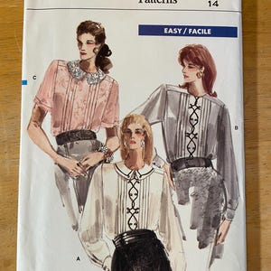 May include: Vogue Patterns sewing pattern for a blouse, size 14. The pattern shows three different styles of blouses with a collar and a decorative tie detail. The pattern is labeled "Easy/Facile".