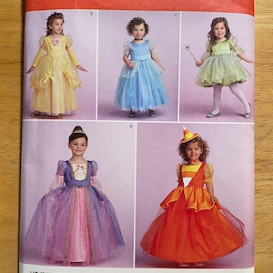 May include: Simplicity sewing pattern 1303 for children's costumes. The pattern features various princess and fairy tale-themed dresses in yellow, blue, green, purple, and orange. The size range is Euro 3-6.