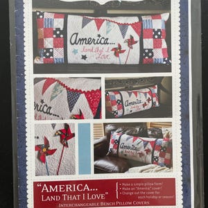 May include: A Kimberbell KD177 sewing pattern for an interchangeable bench pillow cover measuring 16 by 38 inches. The design features a red, white, and blue patchwork quilt style with the text America... land that I Love and pinwheel accents.