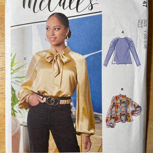 May include: McCall's sewing pattern M8147 featuring a woman wearing a gold satin blouse with a bow. The pattern includes multiple view options with simple instructions. The size is Y (XS-S-M).