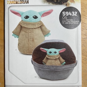 May include: A sewing pattern featuring a plush Grogu and soft space pram. The pattern includes images of the Grogu plush toy in a tan coat with large ears and a gray pram. The Star Wars Mandalorian logo is at the top.