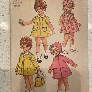 May include: Vintage Simplicity sewing pattern #9191 for a toddler girl's dress and coat. The pattern includes instructions for a yellow dress with a Peter Pan collar, a pink coat with a hood, and a white dress with a floral print.