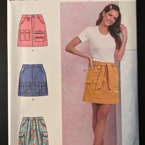 May include: Simplicity sewing pattern S9924 featuring a woman wearing a mustard-colored skirt with pockets. The pattern includes illustrations of skirts in pink, blue, and floral prints. The size range is U.S. 16-24.
