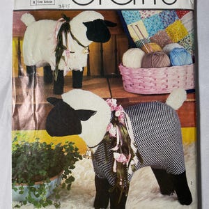 May include: A Simplicity Crafts sewing pattern envelope for a stuffed sheep, number 353. The cover features two sheep figures with black heads and legs, one with a white fleece body and one with a black and white houndstooth patterned body.