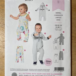 May include: A Burda Kids sewing pattern envelope 9299 for children's jumpsuits. The package displays two styles: a sleeveless jumpsuit with a colorful fruit print and a long-sleeved hooded jumpsuit in grey with a cat face graphic and whiskers.