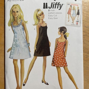 May include: Simplicity sewing pattern S9594. The pattern features illustrations of three dresses: a light blue dress, a black dress, and a red dress with white floral patterns. The pattern includes size information and the text "Jiffy".