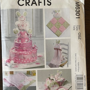 May include: Sew Sweet Chic by Susan Cousineau sewing pattern for a baby shower gift set. The pattern includes instructions for making a nappy cake, a hooded towel, a blanket, and a bunny-shaped quilt. The pattern is printed on a white background with pink and green accents.