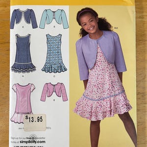 May include: Simplicity sewing pattern 2470 for girls' dresses and boleros. The pattern features different dress styles with ruffled hems and bolero jackets. The image shows a girl wearing a floral dress and a purple bolero. Sizes AA 8, 10, 12, 14, 16.