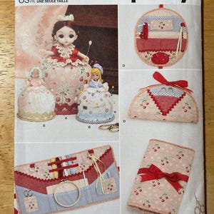 May include: Simplicity sewing pattern S9809. The image shows doll-shaped pincushions and sewing accessory organizers. The pattern features cherry patterns and red accents. The text "Designed and printed in USA" is visible.