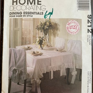 May include: A McCall's Home Decorating pattern for dining essentials, featuring a white tablecloth and chair covers with ruffles and bows. The pattern number is 9212.