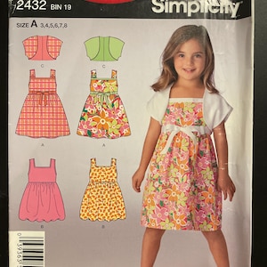 May include: A Simplicity sewing pattern envelope 2432 for a dress and bolero jacket. The cover features illustrations of four dress variations and two bolero styles, along with a photograph of a dress with a floral print and white bolero.