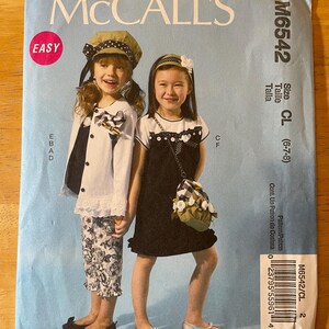 May include: A McCall's sewing pattern for girls' clothing, size CL (6-7-8). The pattern features two girls wearing different outfits, one with a white jacket and floral pants, and the other with a black dress and a floral bag. The pattern is labeled "Easy" and includes instructions for making both outfits.